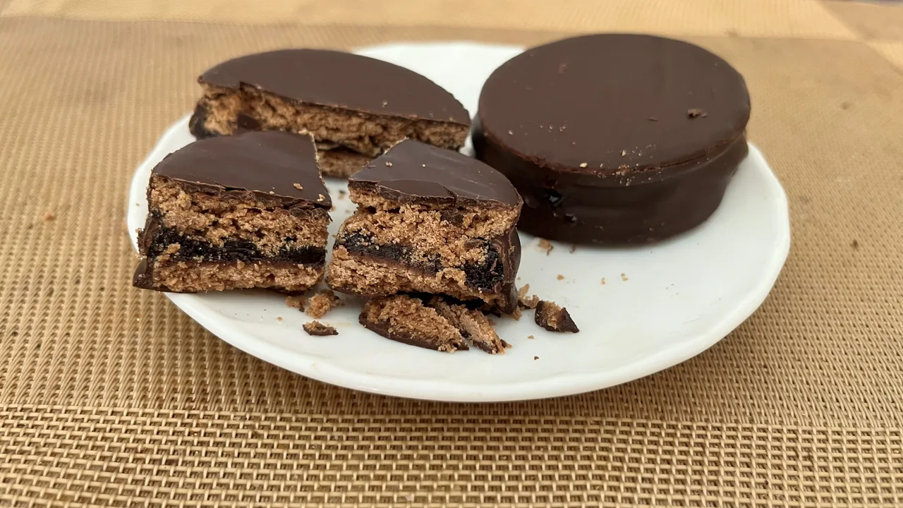 Een alfajor doormidden gesneden: de cacaokoekjes, de donkere calafatevulling ertussen en de dikte van de chocoladelaag