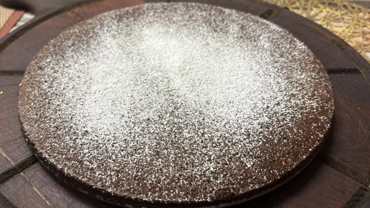 Kokonainen kladdkaka puualustalla, tomusokerilla koristeltuna.