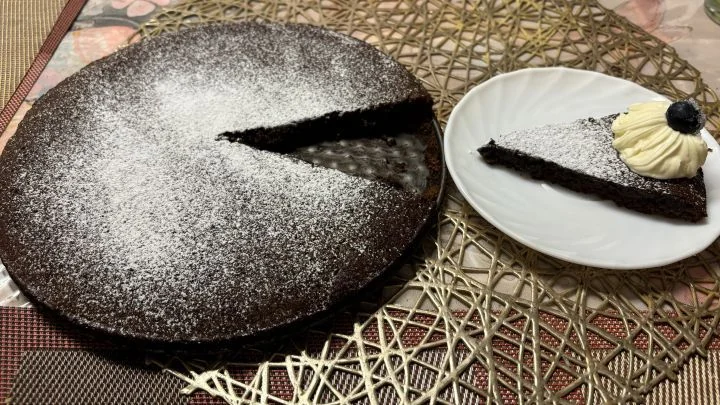 Leikattu kladdkaka, annos lautasella kermavaahdon ja mustikan kera.
