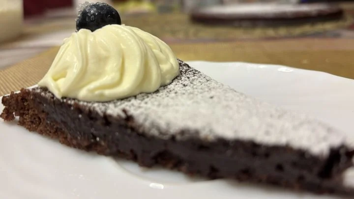 Lähikuva kladdkaka-palasta, jossa näkyy tiivis sisus, kermavaahtoa ja mustikka.