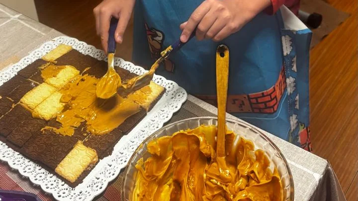 Espalhando recheio de doce de leite e queijo cremoso sobre camada de biscoitos de chocolate