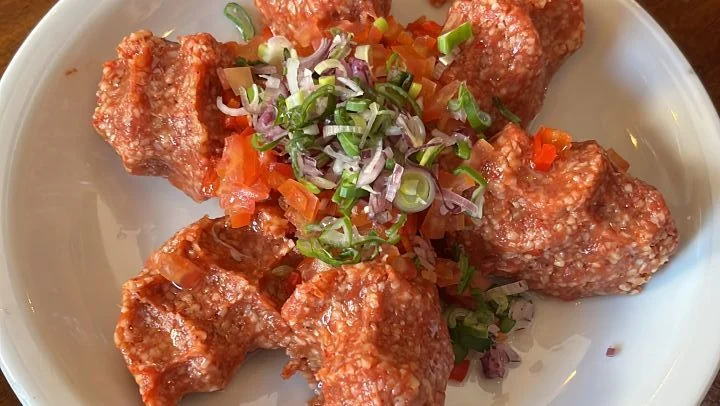 Die Chi-Köfte-Portionen mit dem Abdruck der Finger, rund um eine Mitte aus gehackten Tomaten, roten Zwiebeln und Frühlingszwiebeln