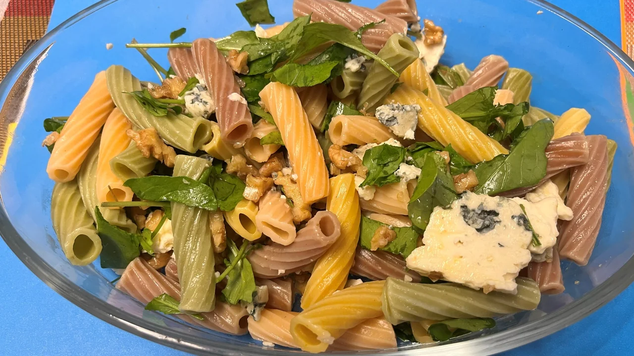 Salada morna de macarrão curto com rúcula, nozes e queijo azul em uma tigela de vidro