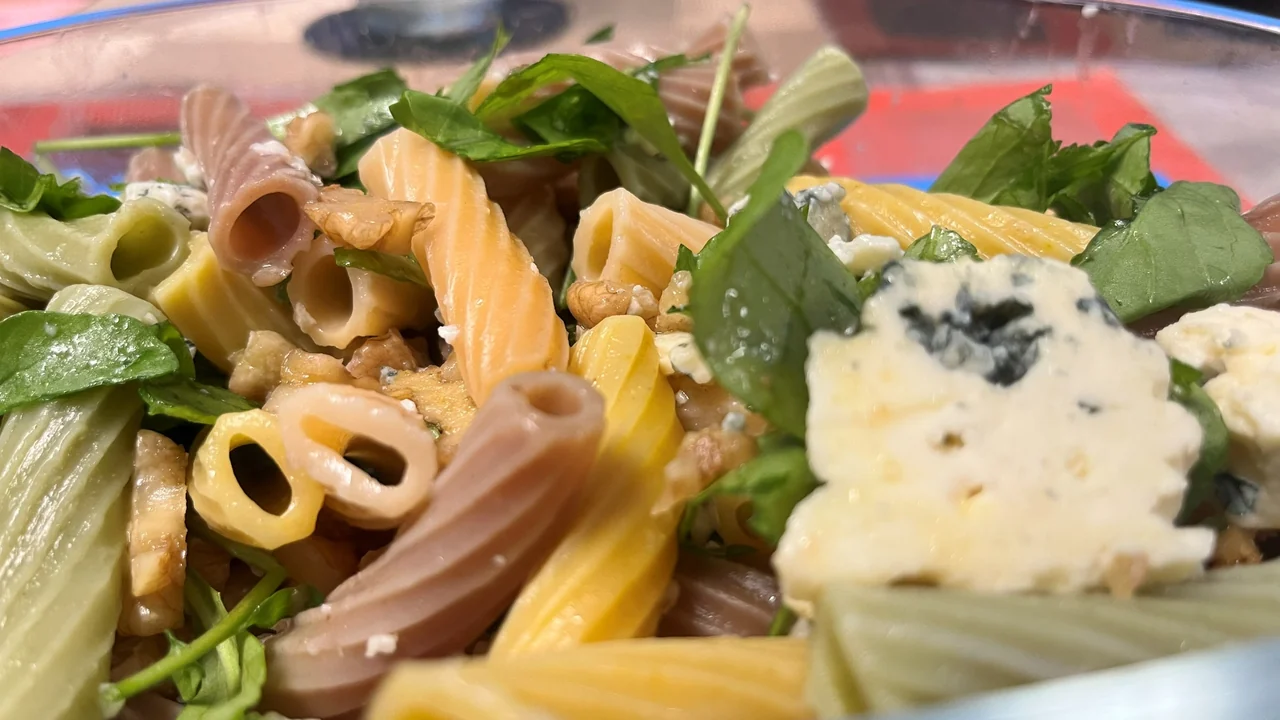 Close do queijo azul em pedaços, das nozes e da rúcula entre o macarrão morno