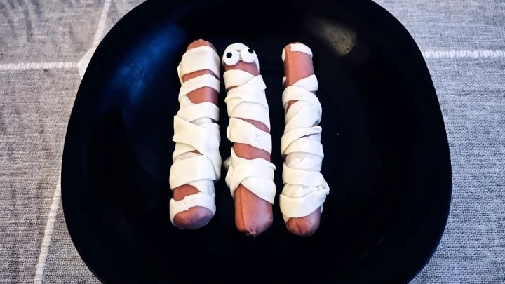 Kolme raakaa nakkia käärittynä lehtitaikinasuikaleisiin ennen paistamista; keskimmäisellä on jo silmät, mitä ei tule tehdä.
